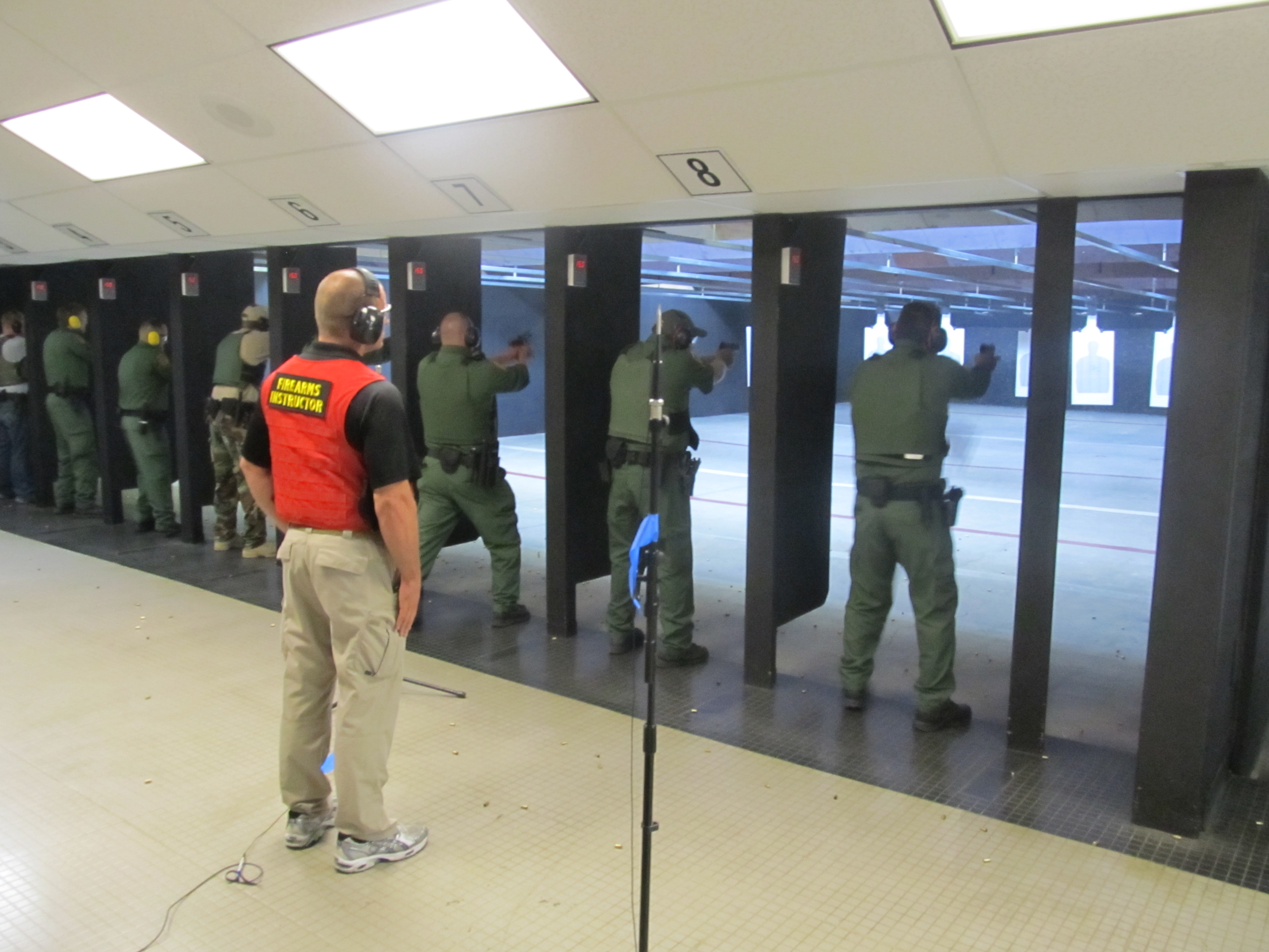 Treino de tiro em estande indoor, com atiradores nas baias.